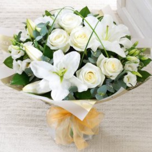 White lilies, roses and lisianthus expertly arranged in a hand tied bouquet